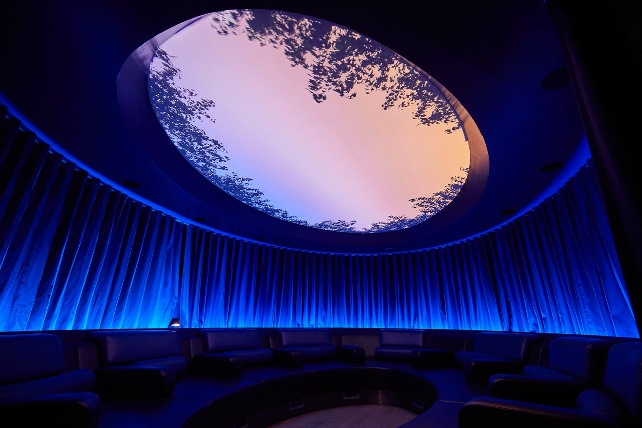 Forest Meditation room lined with comfortable seating and a glass dome on the ceiling to observe the sky lined with tree branches.